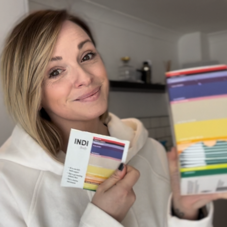 Person holding packages and smiling at the camera indoors.